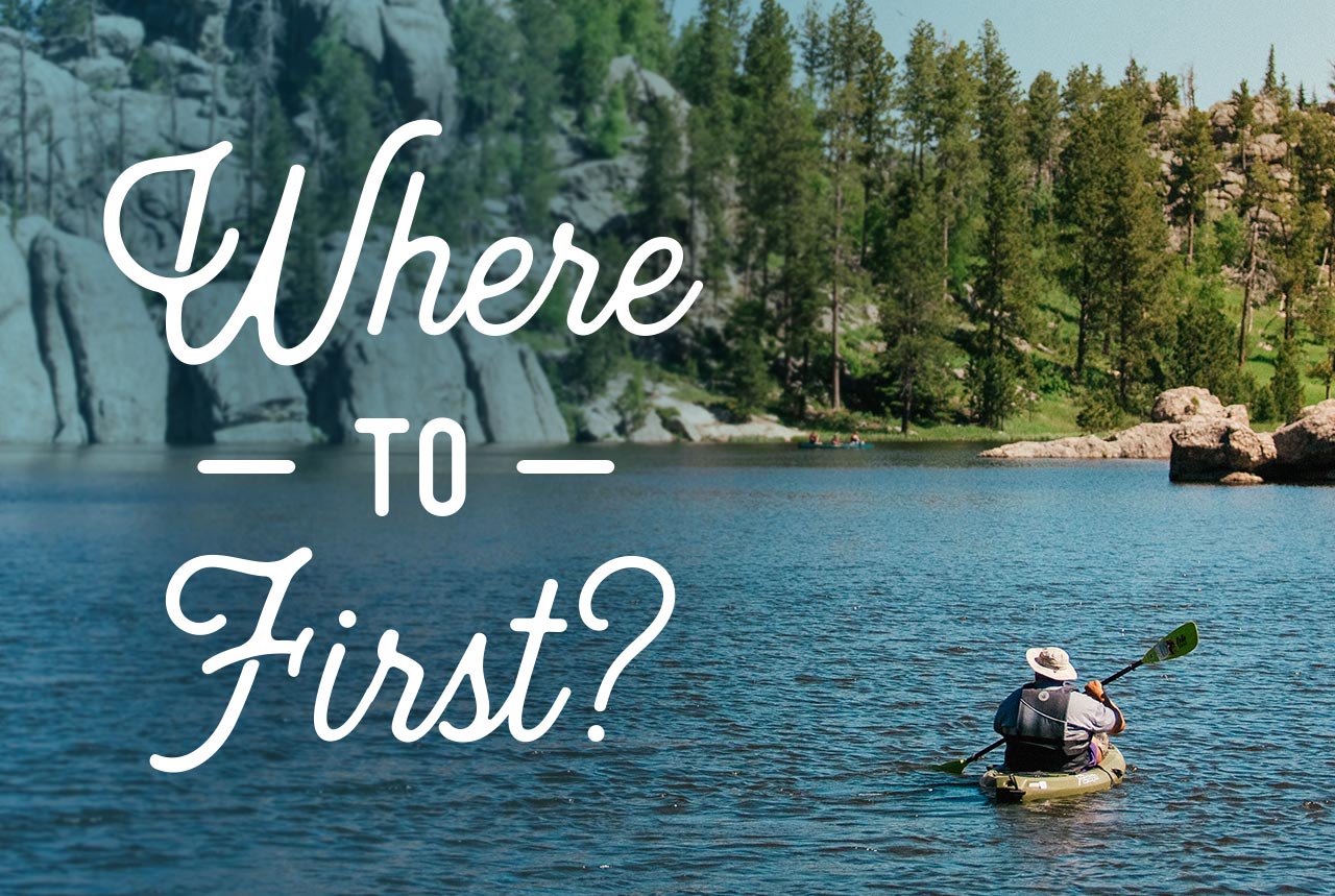 Where to First? - A man kayaking in a river with rocks in the distance.